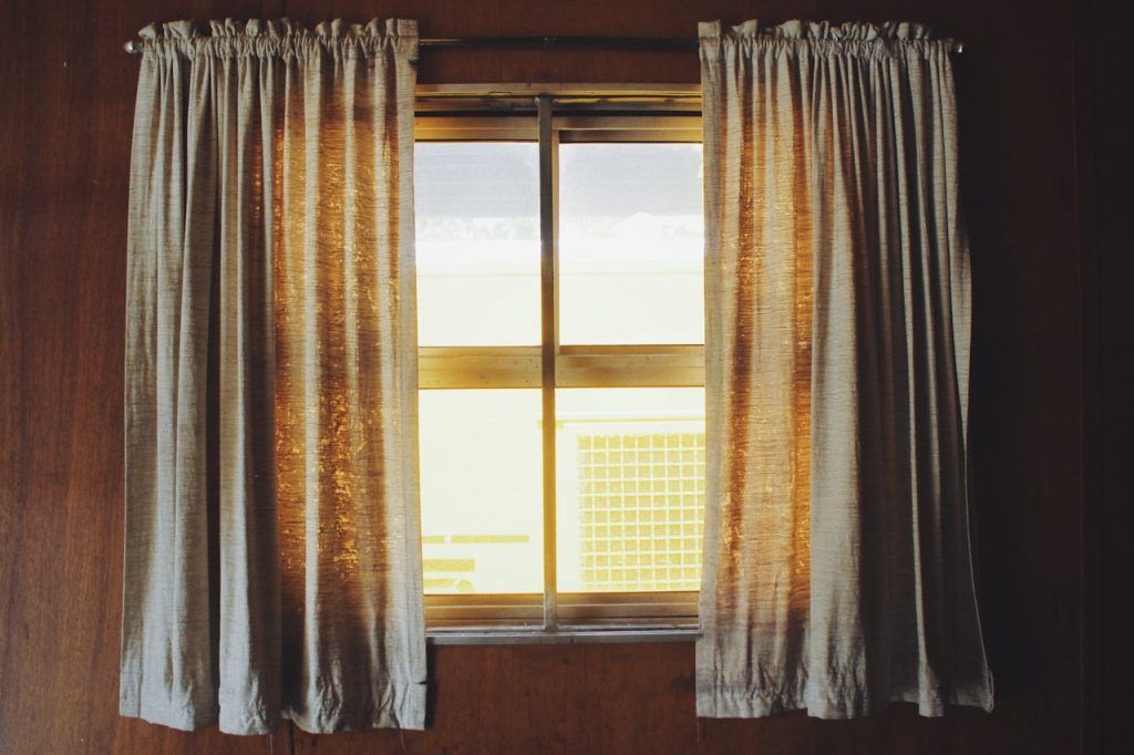 Warm sunlight streaming through fabric curtains in a wooden interior setting.
